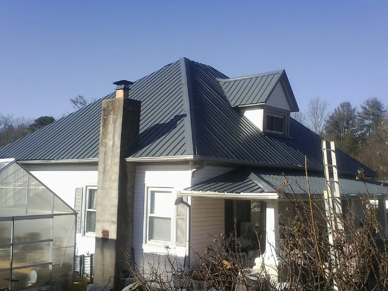 Dark blue standing seam metal roof on a white farmhouse with dormer — Slate & Tile Roof Repair by Roofing Brothers in Random Lake