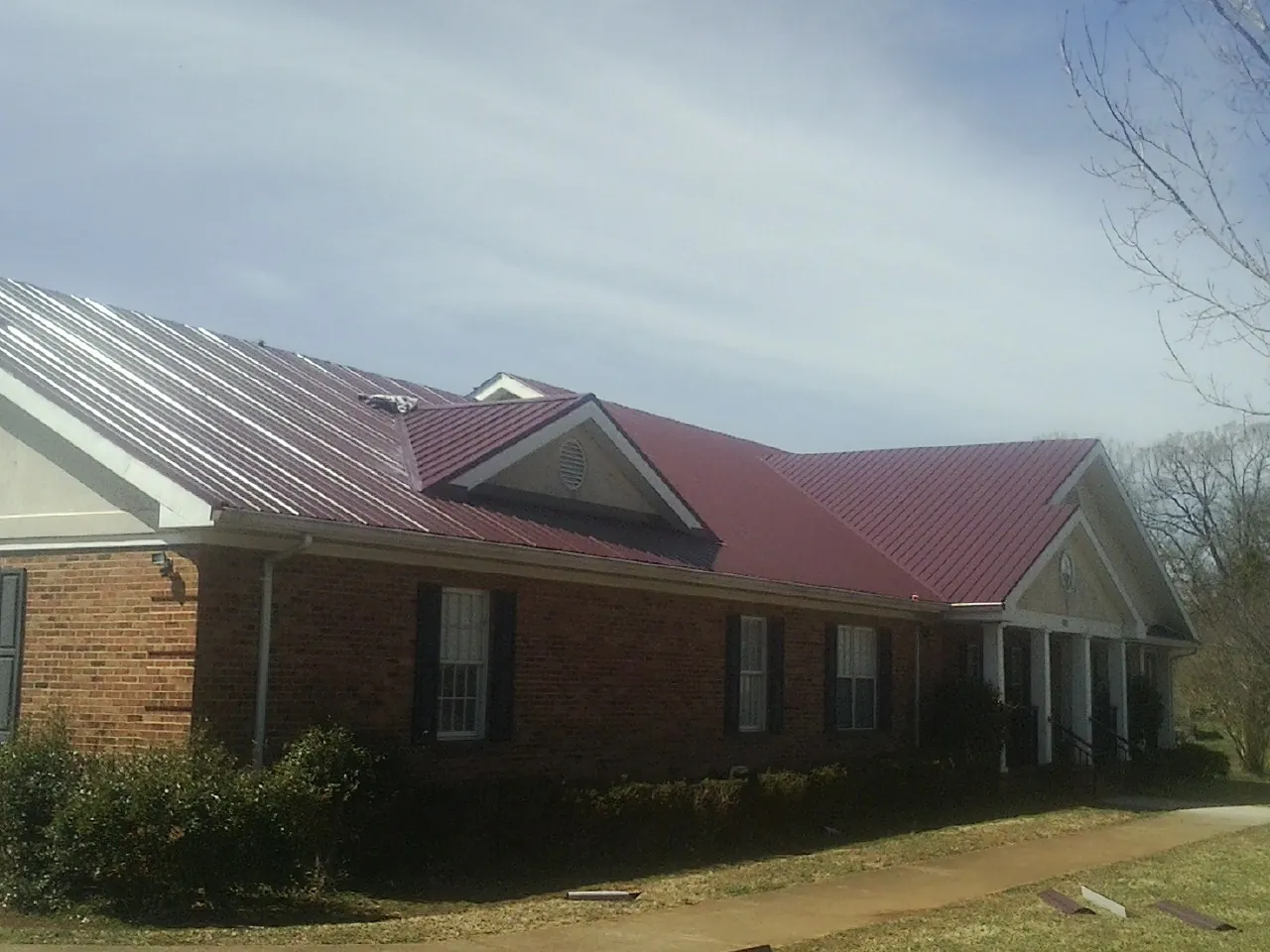 Red metal roof with gabled entries on a long brick building, from a Hail Damage Roof Repair job in Random Lake