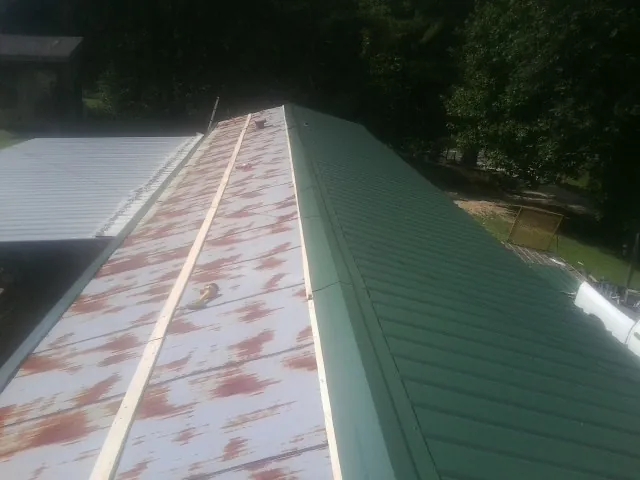 Old rusted panels beside newly installed green metal roofing — Wind Damage Roof Repair by Roofing Brothers in Random Lake