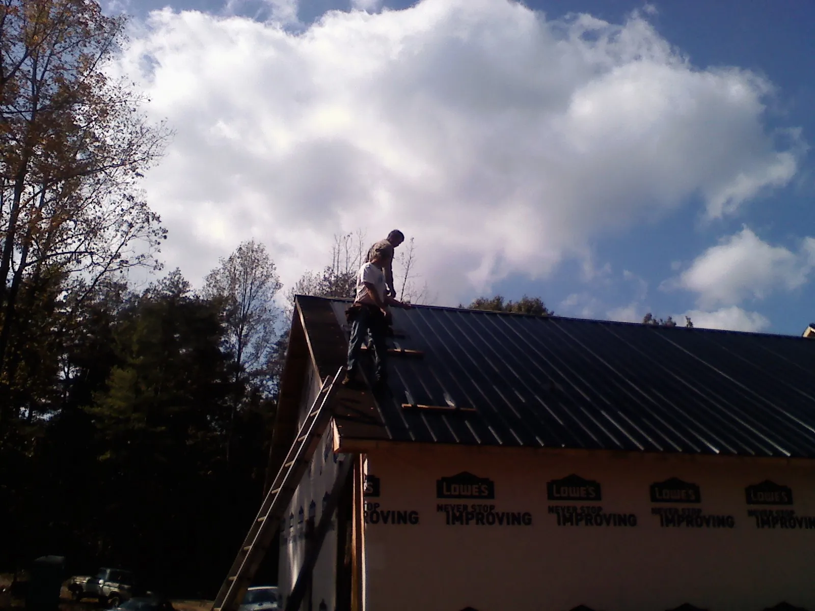 Roofer fastening dark metal panels high against a cloudy sky, from a Roof Inspection job in Random Lake