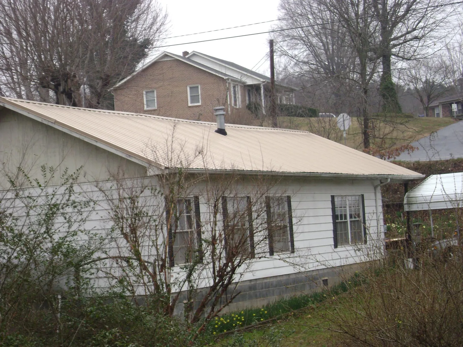 Tan metal roof on a white sided house set into a hillside — Commercial Roofing by Roofing Brothers in Random Lake