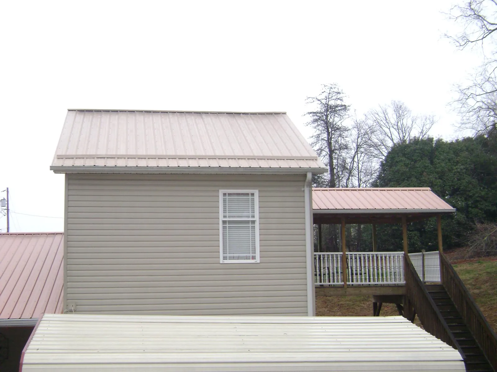 Tan metal roofs on a two story addition and attached porch, from a Roof Replacement job in Random Lake